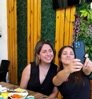 Dos clientas sacándose una foto en una mesa junto al muro verde